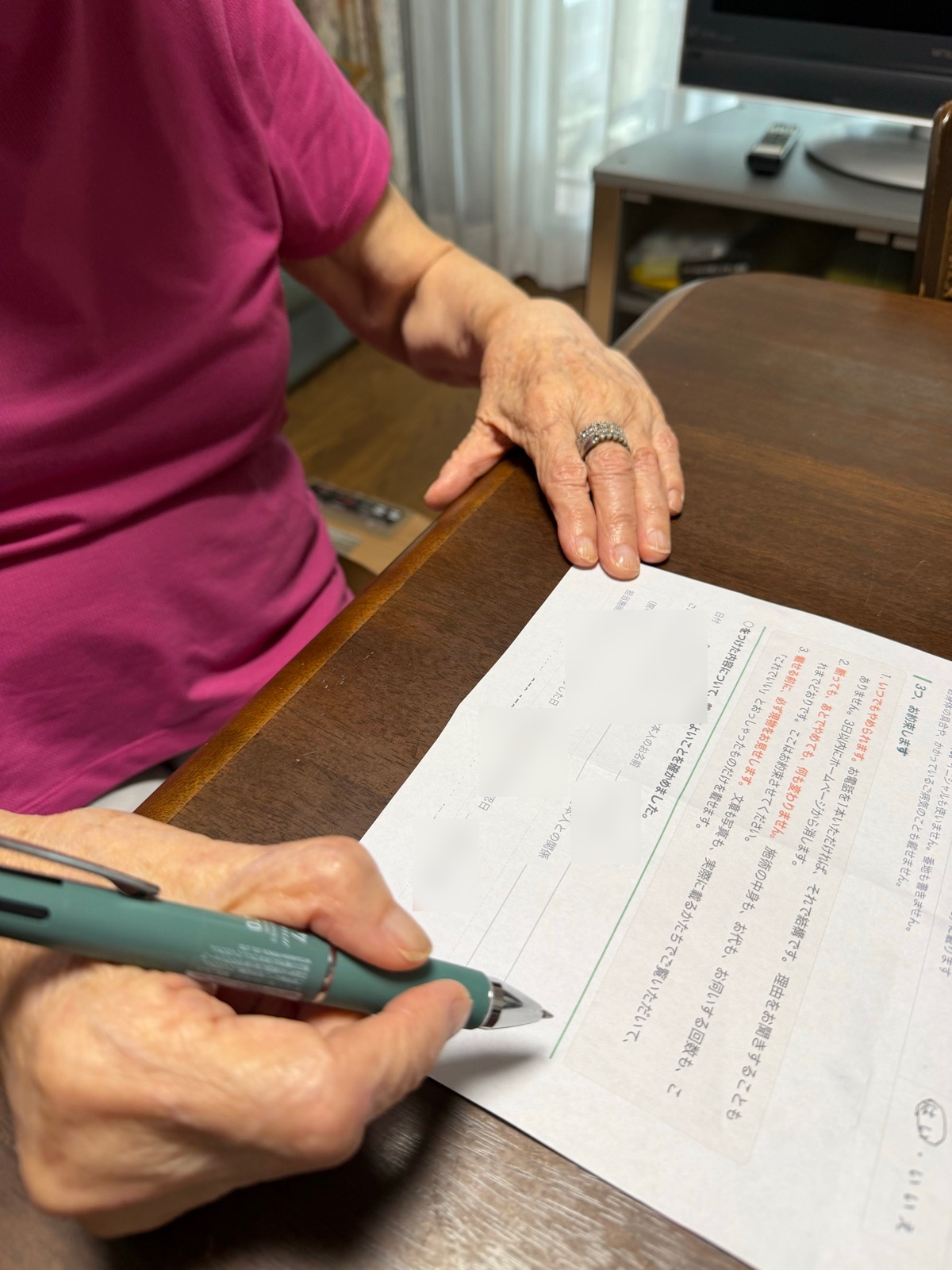 テーブルに向かって座り、ペンを持って書類に記入している利用者さんの手元。お顔は写っていません