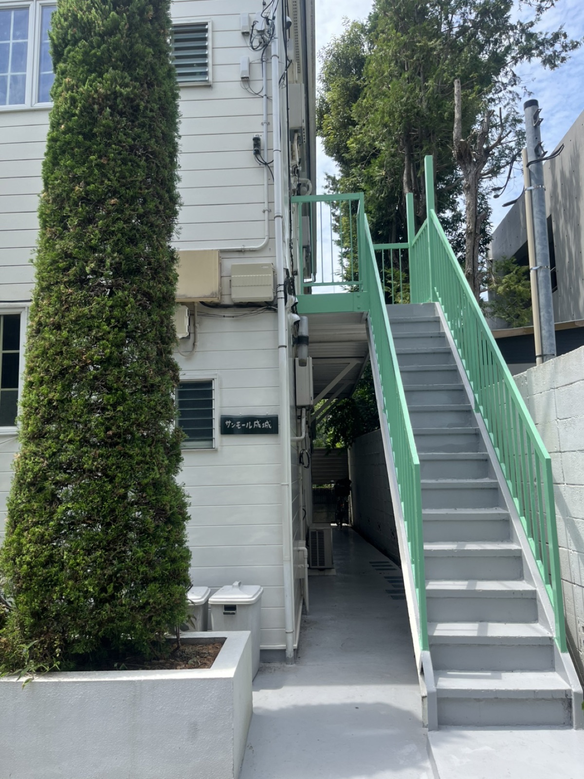 建物脇の通路と緑色の外階段。1階の通路の奥が入口です